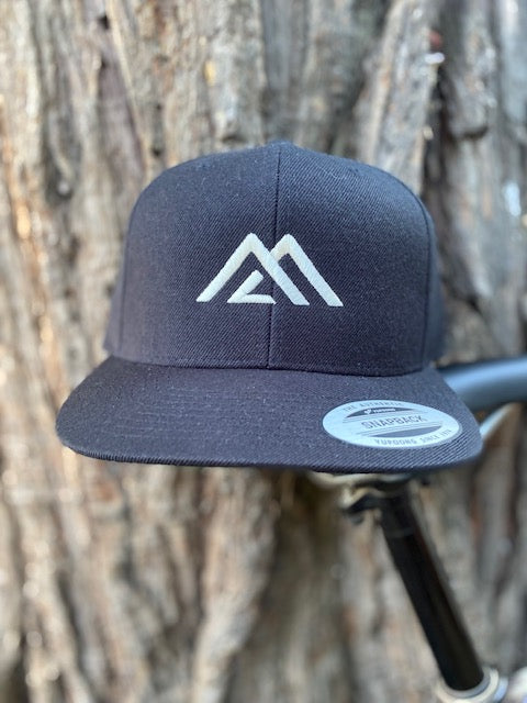 Peaks Logo for Mountain Life Supply co, Black and Cream structured snapback hat against a tree